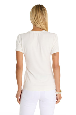 A woman with long blonde hair, seen from behind, wears the Amaya Ultra Soft T-Shirt - Crystal Anchors and white pants against a white background. She has a tattoo on her left upper arm and a bracelet on her right wrist.