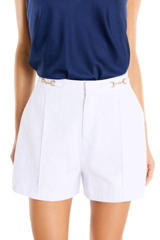 A woman is shown from torso to upper legs wearing a navy blue sleeveless top tucked into white Ellery Horsebit Shorts, which feature gold horsebit hardware at the waistband.