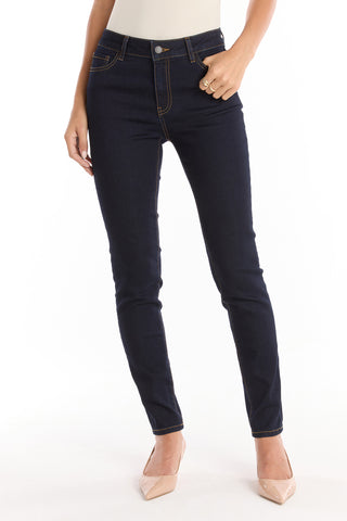 A person wearing Layla Skinny Jean - Indigo and nude pointed-toe heels stands against a white background, one hand on their hip, the other by their side.