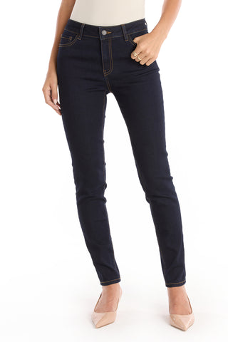 A person wears Layla Skinny Jean - Indigo, made from stretch denim, and beige pointed-toe heels while standing against a white background with one hand in a pocket. The upper body is not visible.
