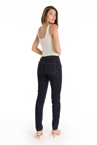 A woman stands facing away, looking over her shoulder. She wears a white sleeveless top, beige heels, and the Layla Skinny Jean - Indigo with visible stitching, set against a plain white background.