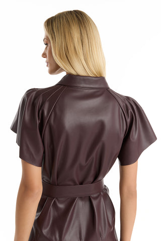 A woman with straight blonde hair is shown from the back, wearing the Devin Leather Ruffle Dress in merlot, featuring short sleeves and a belted waist, against a white background.