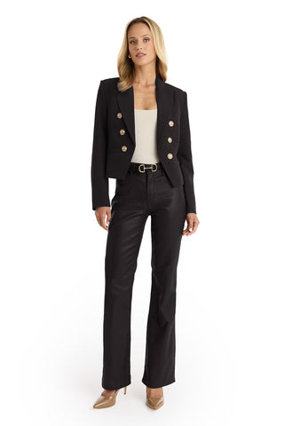A woman wears the Gabrielle Double Breasted Blazer - Black with black pants, a white top, a black belt with a gold buckle, and beige heels, standing against a white background.