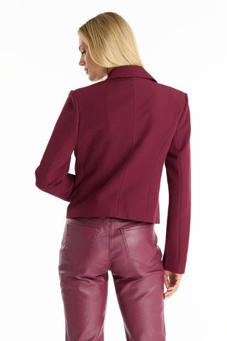 A woman with straight blonde hair models the Gabrielle Double Breasted Blazer in Merlot and matching leather pants, facing away to reveal the back of her outfit against a plain white background.