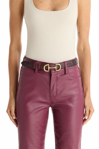 A person wears a sleeveless off-white top tucked into high-waisted burgundy leather pants, accessorized with the Bettie Belt - Merlot featuring a gold horsebit design. Only their torso and upper legs are visible.