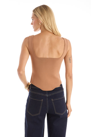 A woman with straight blonde hair faces away, wearing a sleeveless Venus Button Top - Mocha Mousse with a square neckline and dark blue jeans. Gold hoop earrings, bracelets, and a visible arm tattoo complete her effortless summer look.