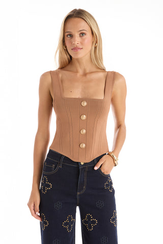 A woman with long blonde hair wears the Venus Button Top in Mocha Mousse, a corset-inspired, sleeveless top with a square neckline and vertical seams, paired with dark denim jeans featuring gold studs and decorative patterns.