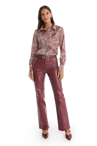 A woman stands facing forward in the Paulina Silk Blouse - Burgundy Zebra, paired with burgundy leather belted pants and matching heels against a simple white background.