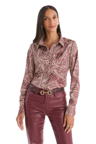 A woman stands against a white background wearing the Paulina Silk Blouse in Burgundy Zebra, paired with high-waisted burgundy leather pants and a black belt with a gold buckle.