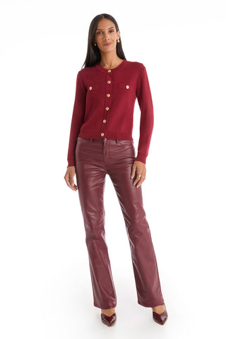 A woman with long dark hair stands against a white background wearing the Loretta Knit Cardigan Top in Merlot, paired with burgundy leather pants and matching pointed heels. She faces forward with a neutral expression.