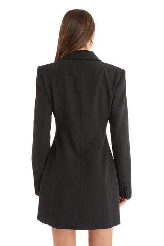 A woman with long brown hair is shown from the back wearing the Kira Blazer Dress in black, featuring power shoulders and long sleeves, against a plain white background.