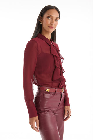 A woman with long dark hair wears the Georgia Semi-Sheer Blouse in burgundy, standing against a plain white background and looking confidently at the camera.