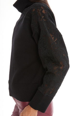 A person wearing the Camille Lace Turtleneck Sweater in black, featuring semi-sheer lace sleeve detailing and ribbed cuffs, paired with high-waisted burgundy pants, shown from the side against a white background.