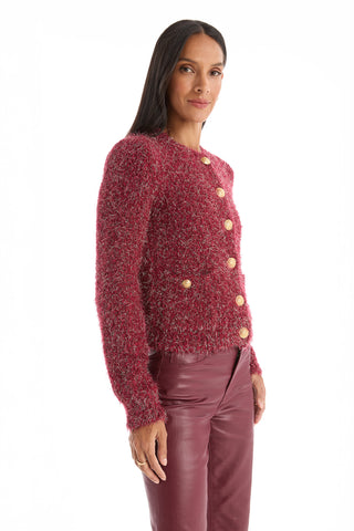 A woman with long, straight dark hair and a calm expression poses against a white background wearing the Joana Knit Cardigan - Merlot, featuring textured knit fabric, padded shoulders, large buttons, and matching maroon leather pants.