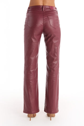 A person wears Aria Coated Flare Jean in Merlot, featuring a high-rise fit with back pockets. The photo shows only their lower back and legs against a white background.