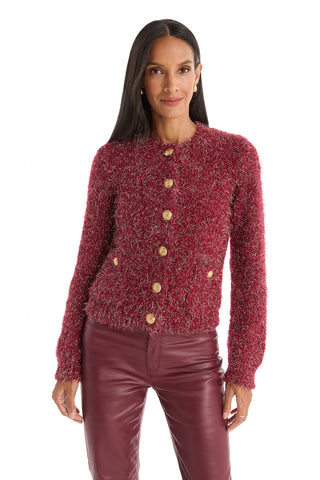 A woman with long dark hair wears the Joana Knit Cardigan in Merlot, paired with matching burgundy leather pants, standing against a plain white background and smiling softly at the camera.