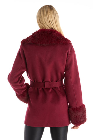 A person with long blonde hair is shown from the back, wearing the Isabel Fur Trim Coat in Merlot, featuring a timeless belted silhouette with faux fur details on the collar and cuffs, paired with black pants.