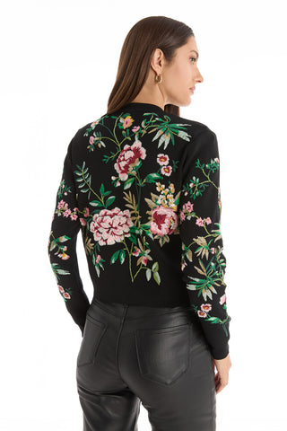A woman with long brown hair models the Alyssa Jacquard Cardigan - Black Floral, featuring colorful floral embroidery, paired with black leather pants, shown from the back against a white background.