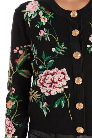 The Alyssa Jacquard Cardigan - Black Floral features gold buttons and colorful embroidered pink, green, and white floral designs on the front and sleeve.