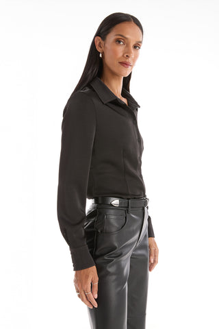 A woman with long dark hair stands confidently against a white background, wearing the Paulina Silk Blouse in black and black leather pants.