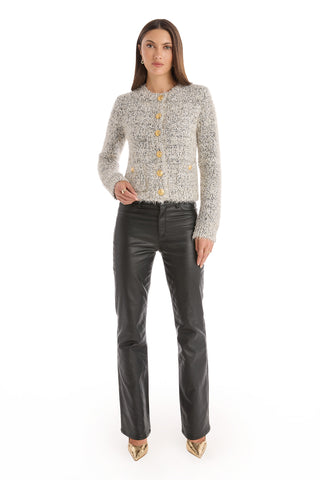 A woman faces forward wearing the Joana Knit Cardigan in grey, styled with black leather pants and gold pointed-toe heels, set against a plain white background.