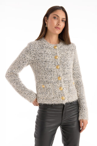 A woman wears the Joana Knit Cardigan - Grey, a fuzzy button-up with gold dome buttons, paired with black leather pants, standing with one hand on her hip against a plain white background.