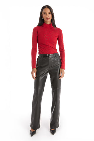 A woman stands facing forward against a white background, wearing the Alina Rose Turtleneck Top in red, black leather pants with a belt, and black pointed-toe shoes.