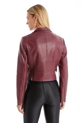 A woman with straight blonde hair, seen from the back, wears the Katalina Moto Jacket - Merlot with a sleek front zip closure and high-waisted black leggings, standing against a plain white background.