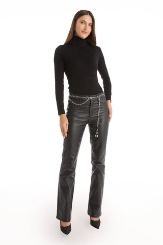 A woman stands against a white background wearing a black turtleneck, black leather pants, and the Arden Chain Belt - Silver. She completes her look with black pointed heels, straight long hair, and a neutral expression.