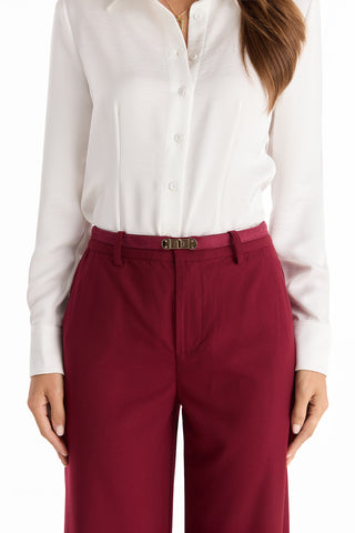 A woman wears a white button-down shirt tucked into Martina Belted Trouser in Merlot, featuring a built-in belt with a gold buckle. Only her torso and upper legs are visible.