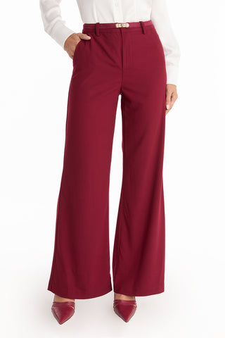 Wearing the Martina Belted Trouser - Merlot, styled with a white blouse and maroon pointed shoes, a person poses with one hand in their pocket against a white background.