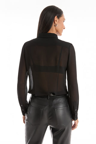 A woman faces away in a Georgia Semi-Sheer Blouse - Black with subtle ruffles and high-waisted black leather pants. Her straight dark hair is tucked behind her ear, set against a plain white background—a standout look.