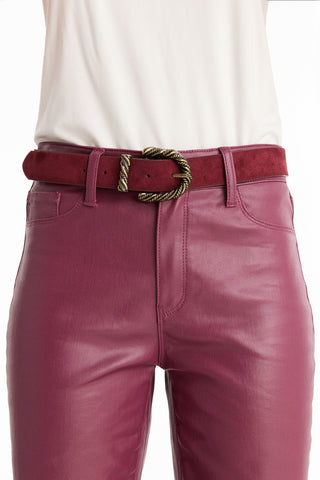 A person wearing high-waisted, shiny magenta pants with an off-white top, styled with the Samantha Belt - Merlot: a maroon suede western belt featuring a twisted gold buckle.