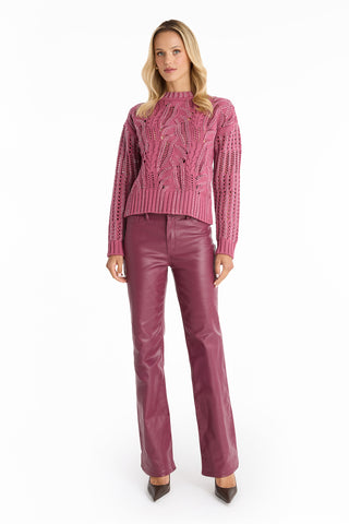 A woman with long blonde hair stands facing forward in the Elea Crystal Knit Sweater in Sangria and shiny maroon high-waisted pants, paired with brown pointed-toe heels against a plain white background.