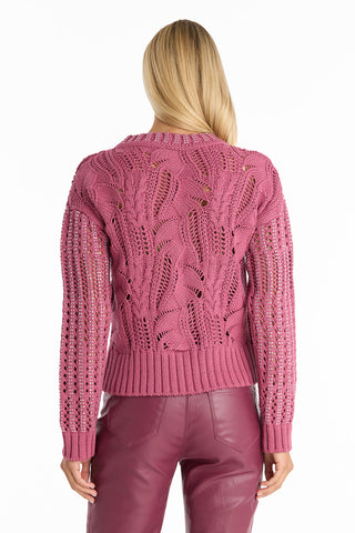 A person with long blonde hair, seen from behind, wears the Elea Crystal Knit Sweater in Sangria with a leaf-like pattern and matching pink leather pants against a plain white background, showcasing this luxurious knitwear ensemble.