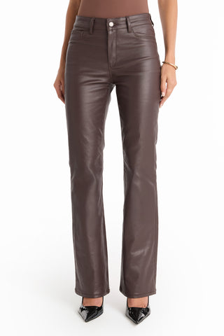 A person wearing high-waisted Aria Coated Flare Jean - Espresso, a fitted brown top, black pointed-toe shoes, and a gold bracelet stands against a plain white background.