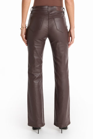 A person stands with their back to the camera, wearing the Aria Coated Flare Jean - Espresso—high-rise brown leather jeans with back pockets and a slim bootcut flare—paired with black heeled shoes.