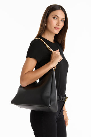 A woman in black holding the Tribeca Chain Leather Bag in black, featuring a gold chain detail.