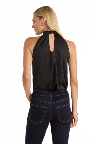 A woman with straight blonde hair models the Rina Tie Neck Blouse in black, featuring a back keyhole detail, paired with dark blue jeans. She stands with her back to the camera against a white background.