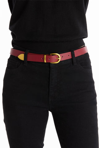 A person wearing black pants and a black top, styled with the Jamie Belt - Merlot, a red faux leather belt featuring a gold hardware buckle—a perfect wardrobe staple.