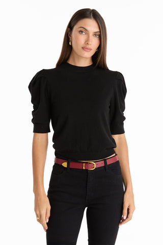 A woman with long brown hair wears the Sylvie Knit Top in black, styled with black pants and a red belt. She stands facing forward against a plain white background, showcasing this chic Fall wardrobe essential.
