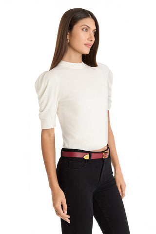 A woman with straight brown hair wears the Sylvie Knit Top in Pearl, featuring puff shoulders, paired with black high-waisted pants and a maroon belt. She stands against a white background—an ideal look for any Fall wardrobe.
