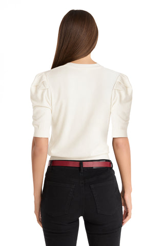 A woman with long brown hair stands with her back to the camera, wearing the Sylvie Knit Top - Pearl, styled with black jeans and a red belt. Her look is chic and modern against a plain white background—perfect for your Fall wardrobe.