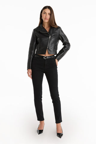 A woman poses confidently in the Katalina Moto Jacket - Black, styled with black jeans, a belt, and pointed-toe heels. Her straight, loose hair completes the look against a plain white background.