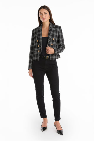 A woman faces forward against a white background wearing the Gabrielle Tweed Double Breasted Blazer in black, styled with a black top, black skinny pants, a black belt with a gold buckle, and black pointed-toe heels.