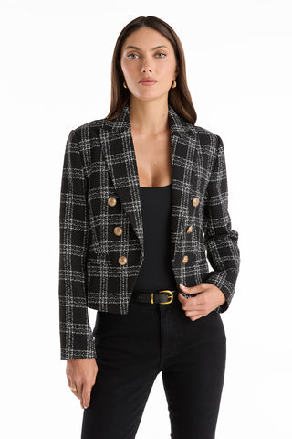 A woman wears the Gabrielle Tweed Double Breasted Blazer - Black over a black top and pants, standing against a plain white background.