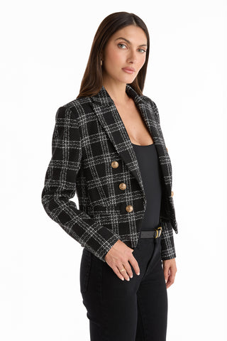 A woman with long brown hair wears the Gabrielle Tweed Double Breasted Blazer in black, styled with a black top and pants, standing against a white background.