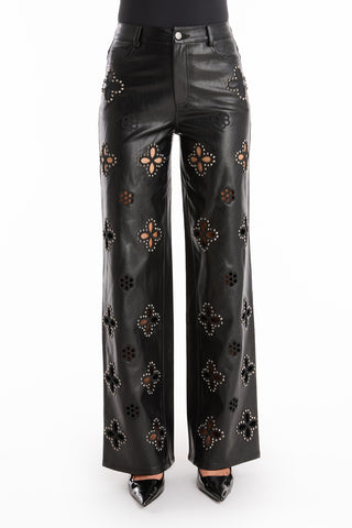 Wearing the Kaia Studded High Rise Leather Pant in black with floral cutouts and silver studs, paired with black pointed-toe shoes. Only the lower half of the body is visible.