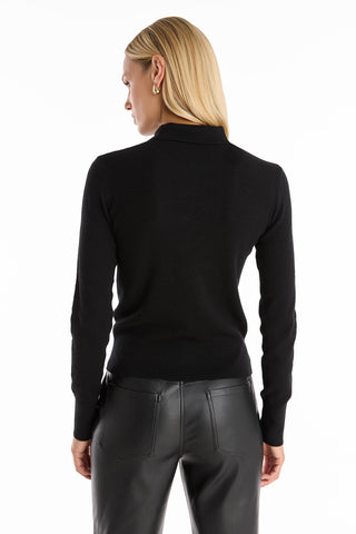 A person with straight blonde hair wearing the Darla Rose Polo Shirt in black and black leather pants stands with their back to the camera against a white background, embodying classic sophistication.