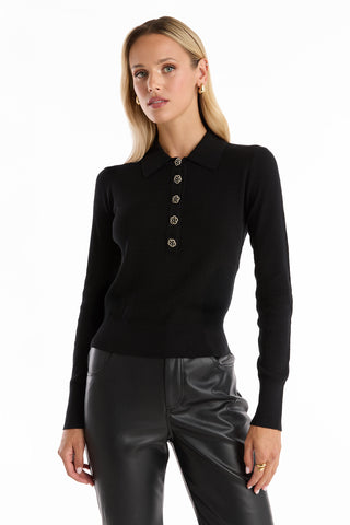 A woman with long blonde hair wears the Darla Rose Polo Shirt - Black with rose-shaped buttons and black leather pants, standing against a plain white background.